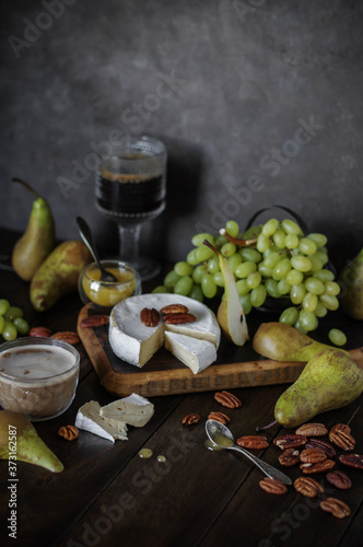 Camembert cheese on a wooden board among fruits, nuts and drinks. Snack table setting. Gourmet food.