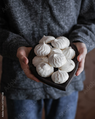 Small meringues on a wooden plate in the hands of a child. Sugar sweets.