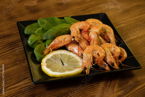 Seafood. Fried roasted shrimps in plate with lemon and greens herbs. Delicious sautéed shrimp on wooden plank, black background photo