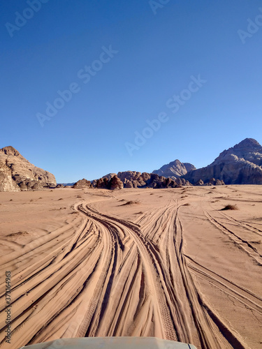 A car drives on a beaten track in the sands of the Wadi Rum desert in Jordan. The pickup truck hood is visible at the bottom of the photo. Clear blue sky. Theme of vacation in Jordan.