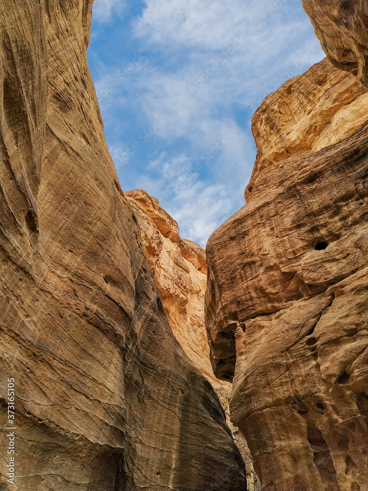 The Siq gorge in Jordan, leading to ancient Petra city. Reddish sandstone cliffs. Blue sky with clouds. Beautiful landscape theme.