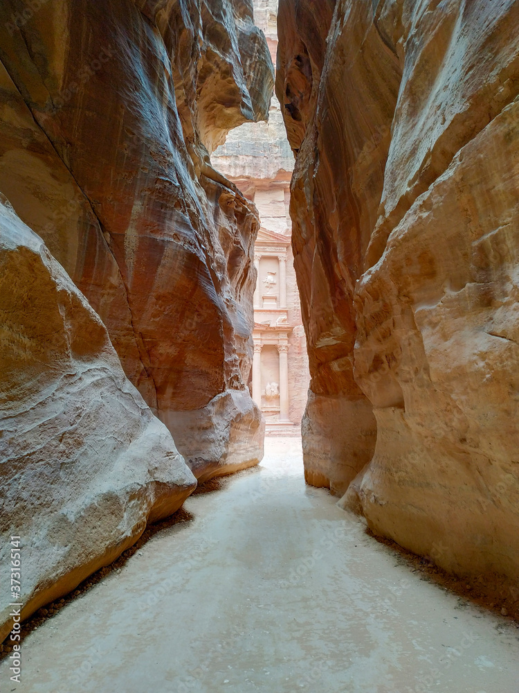 View of temple Al-Khazneh (The Treasury) carved in red sandstone rock through The Siq canyon in ancient Petra city in Jordan. There is no people in front of monument. Beautiful landscape. Travel theme