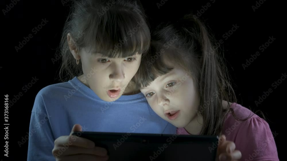 Horror on tablet. Little sisters look at the tablet, the older sister closes the eyes of the younger. Horror on tablet. Little sisters look at the tablet, the older sister closes the eyes of the younger.