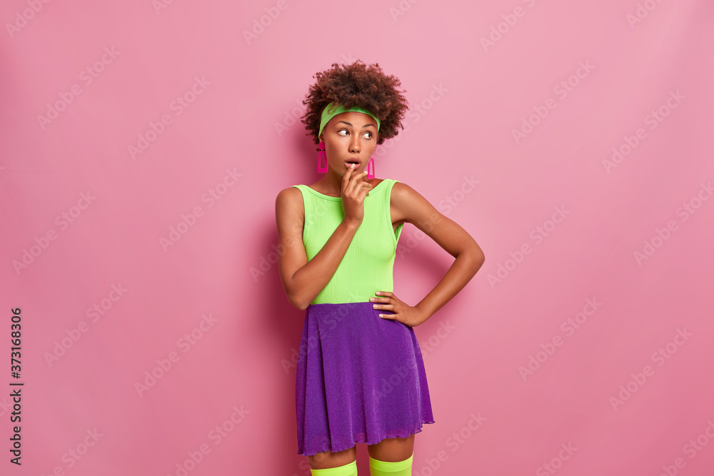Pretty dark skinned young woman looks with wonder aside, dressed in bright clothes, keeps mouth opened, recalls something incredible, poses over rosy background, reacts thrilled on awesome price Pretty dark skinned young woman looks with wonder aside, dressed in bright clothes, keeps mouth opened, recalls something incredible, poses over rosy background, reacts thrilled on awesome price