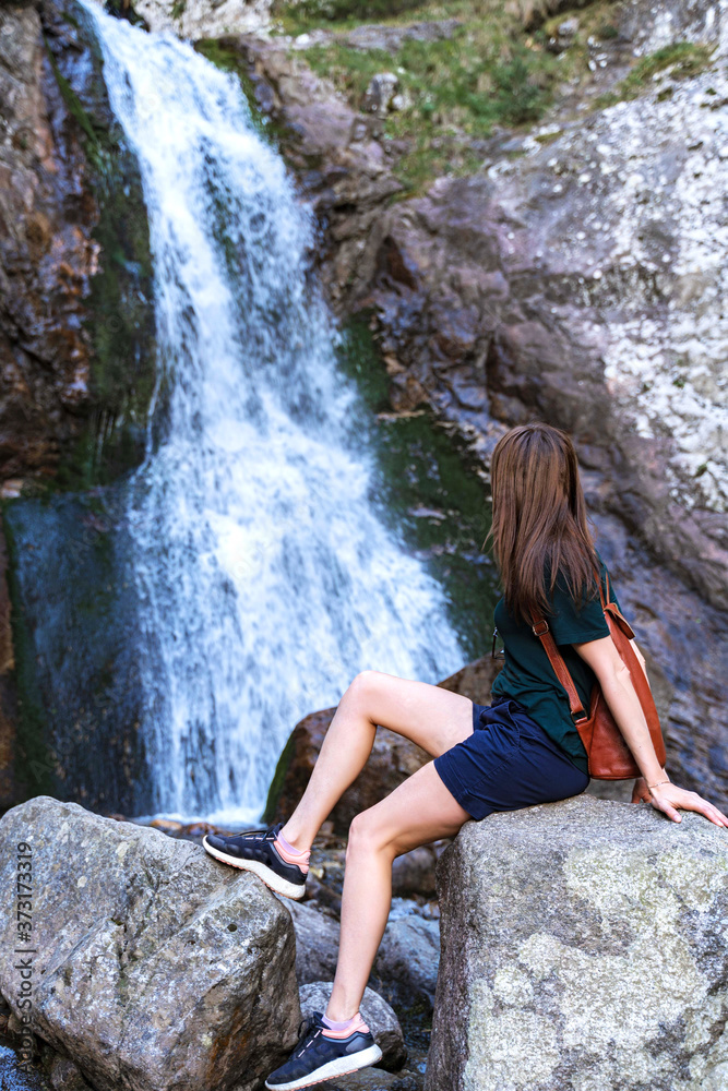 Active healthy girl tourist sitting near the waterfall