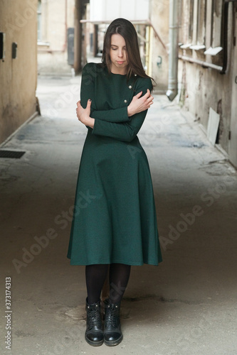 Stylish long-haired Girl in a long green dress freezes in a shabby courtyard...Typical Petersburg courtyard