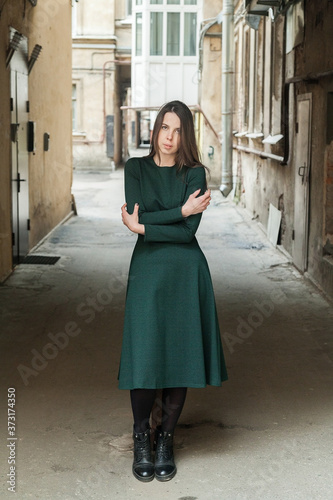 Stylish long-haired Girl in a long green dress freezes in a shabby courtyard...Typical Petersburg courtyard