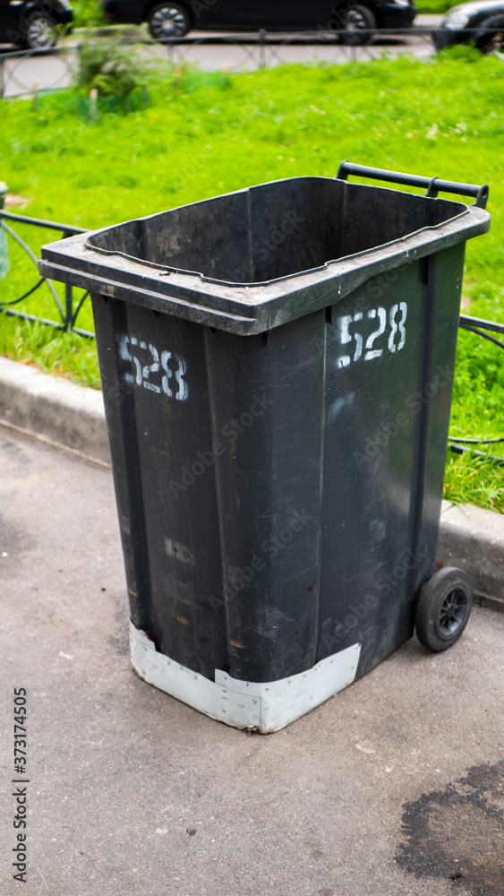 Black plastic garbage collection container on the street with the lid open Black plastic garbage collection container on the street with the lid open