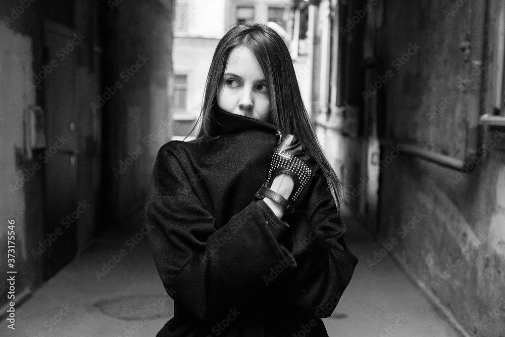 Naklejka premium Long-haired girl in a black coat hides her face in the back streets