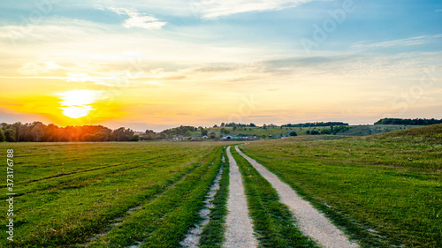 A huge field with a road in the center. And in the distance you can see a small farm at sunset