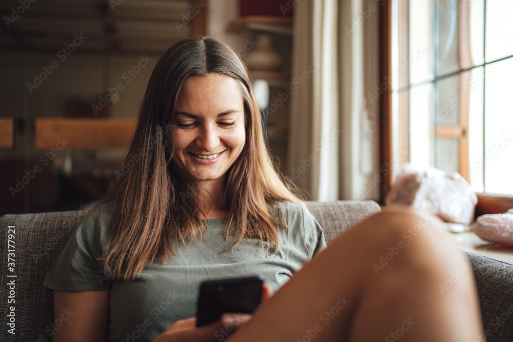 Young brunette woman in casual sitting on sofa at home and using mobile phone Young brunette woman in casual sitting on sofa at home and using mobile phone