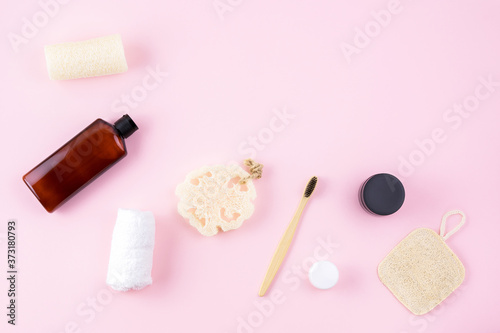 Massager, cream, bottle, loofah sponge scrubbing sponge, bamboo toothbrush on pink surface. Bathroom accessory composition. Wellness zero waste concept. Body care supplies. Top view, flat lay, above.