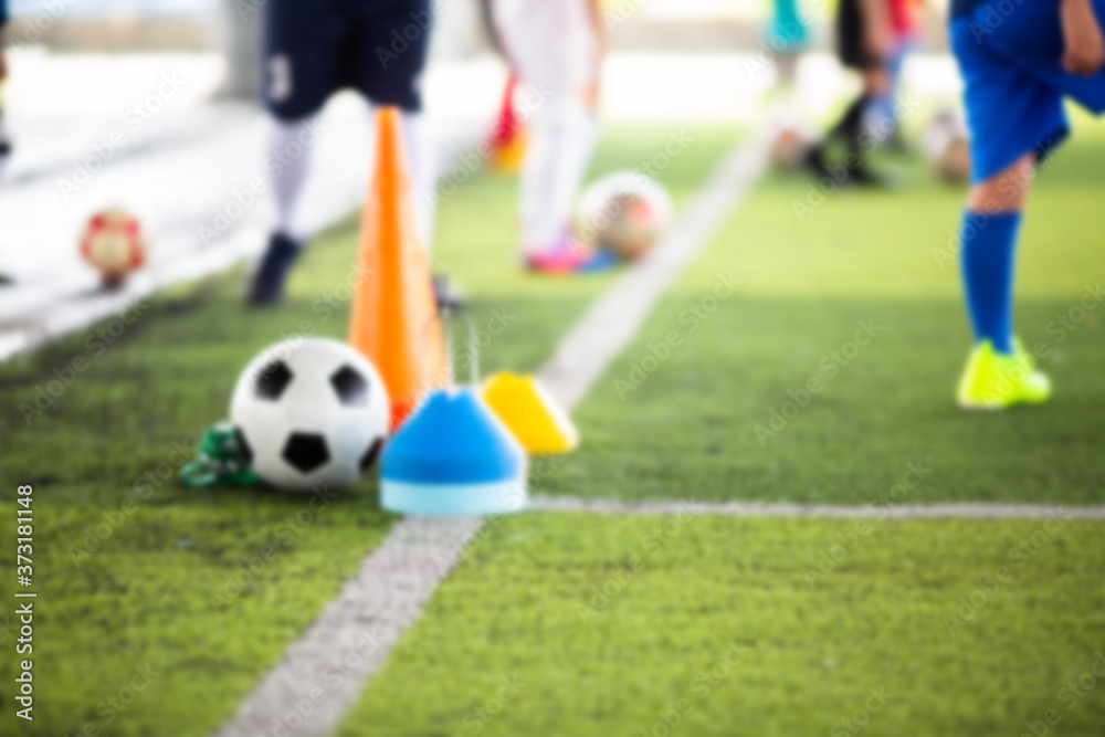 Blurry picture of sport background. Soccer ball with kid soccer player and soccer training equipment on green artificial turf and mini goal in soccer academy.