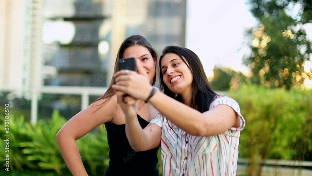 Two young women taking a selfie outside. Millennial girls holding smartphone taking photo Two young women taking a selfie outside. Millennial girls holding smartphone taking photo