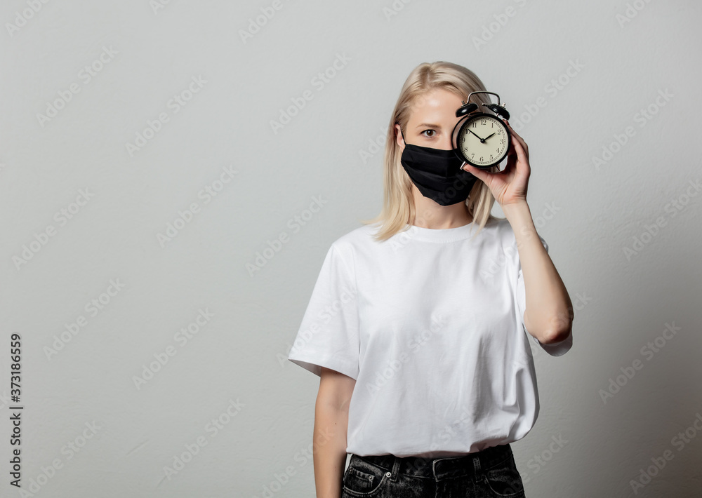 Fototapeta premium Woman in white t-shirt and black face mask with alarm clock on white background