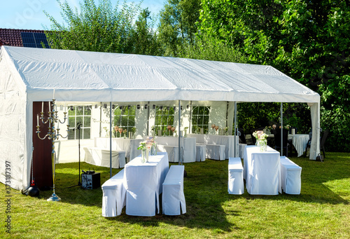 White tent with wedding table setting decorated with fresh flowers , champagne coolers, and decorative glasses for wedding party in a garden photo