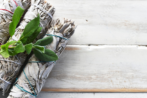 A top view image of white sage smudge bundles with fresh white sage leaves on a white wooden background.  photo