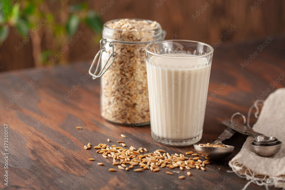 Vegan oat milk, non dairy alternative milk in a glass. Oat flakes on wooden table. Vegan oat milk, non dairy alternative milk in a glass. Oat flakes on wooden table.