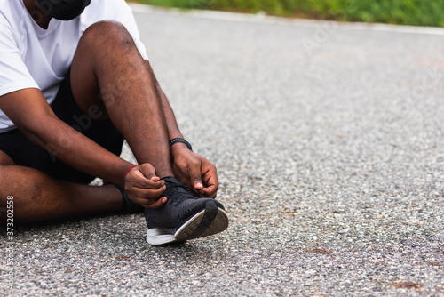 Close up Asian sport runner black man sitting shoelace trying running shoes getting ready for jogging and run at the outdoor street, health exercise workout concept