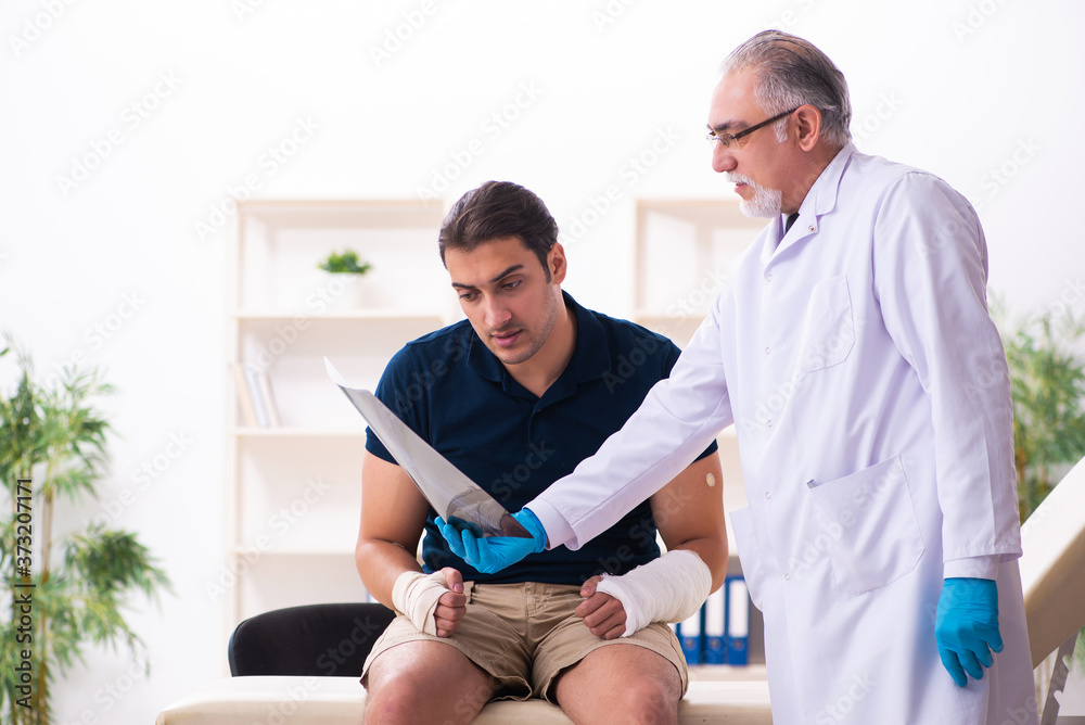 Fototapeta premium Young injured man visiting old doctor traumatologist
