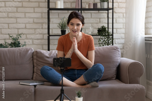 Millennial Caucasian girl blogger influencer sit on couch at home shoot live broadcast on smartphone, young woman vlogger coach talk record video tutorial or training on cellphone, blogging concept