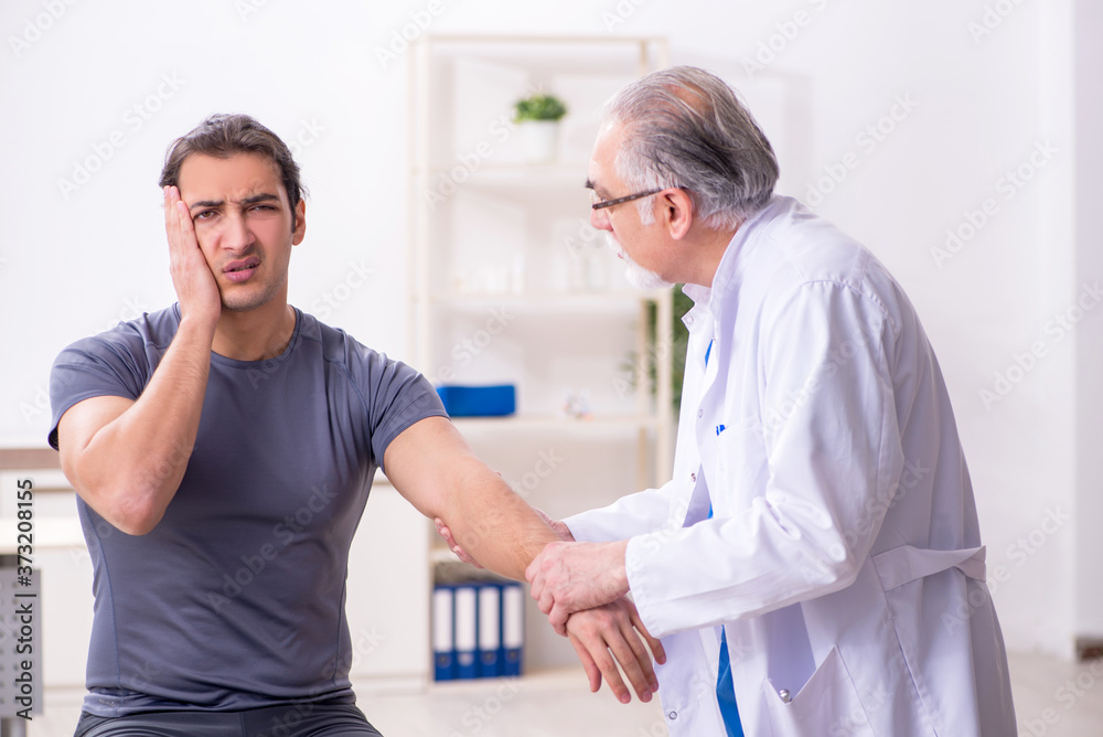Young male patient visiting old doctor traumatologist Young male patient visiting old doctor traumatologist