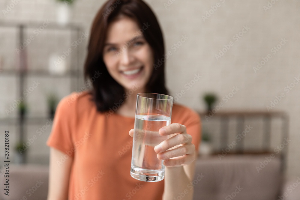 Close up blurred background of young woman stretch hand with glass of clear pure still mineral water, happy millennial girl recommend clean aqua for hydration, refreshment, healthy lifestyle concept Close up blurred background of young woman stretch hand with glass of clear pure still mineral water, happy millennial girl recommend clean aqua for hydration, refreshment, healthy lifestyle concept