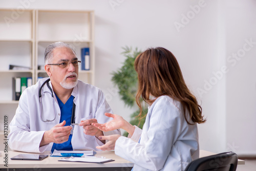 Old male doctor and his young female assistant in the clinic