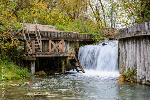 Waterfall and wooden ladder for a descent into the pool with ice water. A source of medicinal water of underground origin on a blue lake in Kazan.