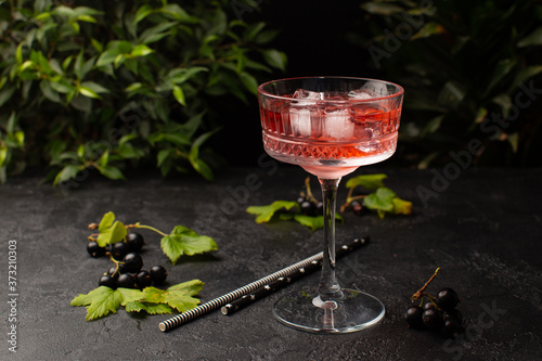 Refreshing summer cocktail with black currant and ice cubes in crystal glass and tropical plants on background.