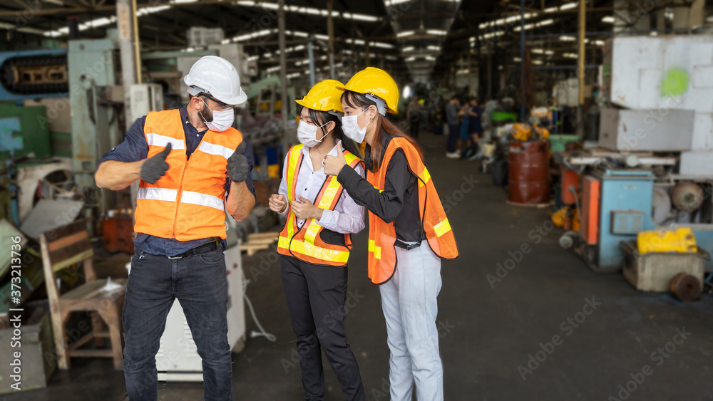 Factory in new normal. Foreman wearing face mask giving explanation to new trainees in a factory warehouse. Male supervisor giving instruction to his co-workers Factory in new normal. Foreman wearing face mask giving explanation to new trainees in a factory warehouse. Male supervisor giving instruction to his co-workers