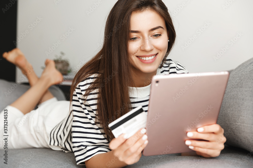 Close-up of resting attractive girl lying couch with digital tablet and credit card, woman relaxing and shopping from comfortable sofa, order online, checking bank account or making internet purchase Close-up of resting attractive girl lying couch with digital tablet and credit card, woman relaxing and shopping from comfortable sofa, order online, checking bank account or making internet purchase