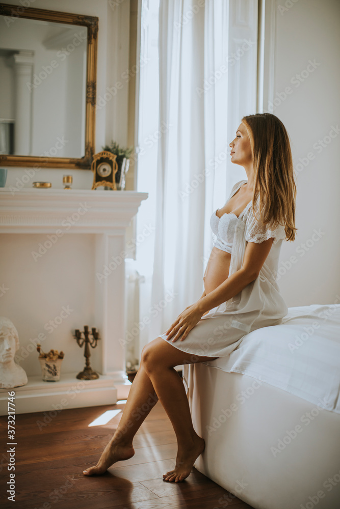 Pregnant woman wearing white  lingerie and posing in the room