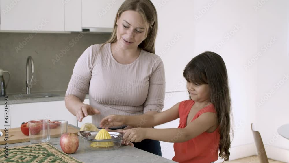 Cheerful mom and little daughter squeezing lemon at kitchen counter, girl drinking sour juice. Medium shot. Family cooking concept Cheerful mom and little daughter squeezing lemon at kitchen counter, girl drinking sour juice. Medium shot. Family cooking concept