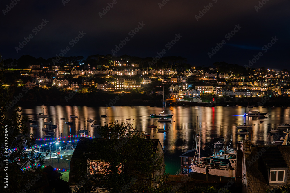 Fototapeta premium town lit up at night with reflection on water with boats