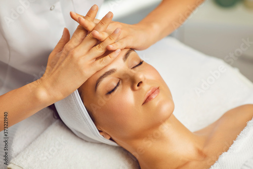 Cosmetologist making facial massage or treatment for young womans face in beauty spa salon