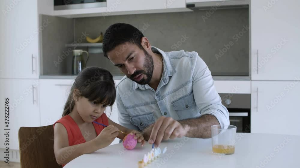 Little girl and her dad painting egg together at dining table. Medium shot, day. Childhood or craft concept Little girl and her dad painting egg together at dining table. Medium shot, day. Childhood or craft concept