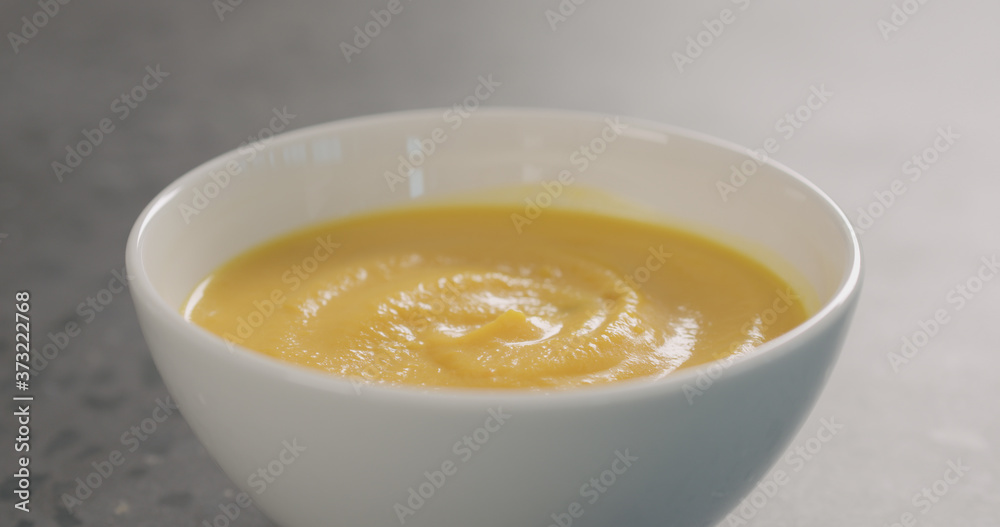 Pumpkin cream soup in white bowl on concrete background Pumpkin cream soup in white bowl on concrete background
