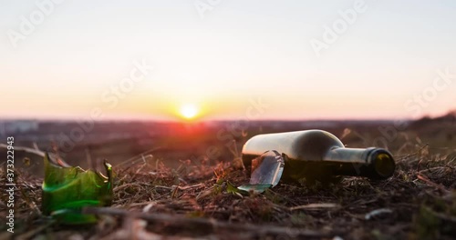 Time-lapse of a bottle next to some glass shards on fertile soil, transitioning from evening to night.