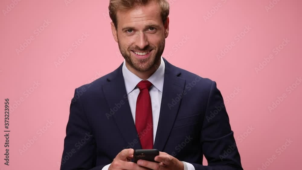 happy elegant fashion man holding phone, reading emails, texting and smiling on pink background happy elegant fashion man holding phone, reading emails, texting and smiling on pink background
