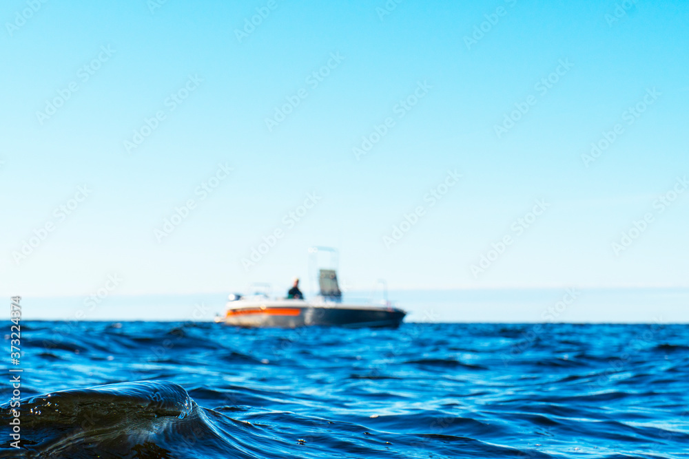 Water surface with blurred fisherman on boat in blue ocean. Beautiful seascape with the blurred fishing boat. Fishing motor boat with angler. Ocean sea water wave reflections.