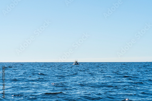 Fisherman on boat in blue ocean. Beautiful seascape with the fishing boat. Fishing motor boat with angler. Ocean sea water wave reflections. Motor boat in the ocean.