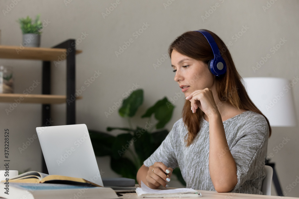 Focused young Caucasian woman in earphones look at laptop screen study online watch webinar on web, millennial female in headphones take internet course training on computer, distant education concept Focused young Caucasian woman in earphones look at laptop screen study online watch webinar on web, millennial female in headphones take internet course training on computer, distant education concept