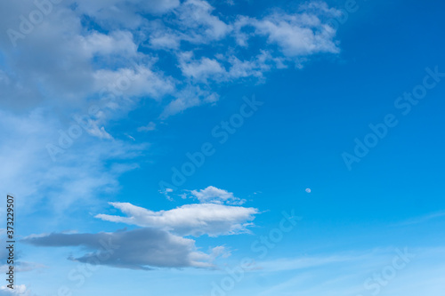 Blue sky with white cloud and visible moon in the daytime.