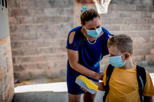 Woman helping her son to be ready to go back to school. They are wearing a protective face mask 