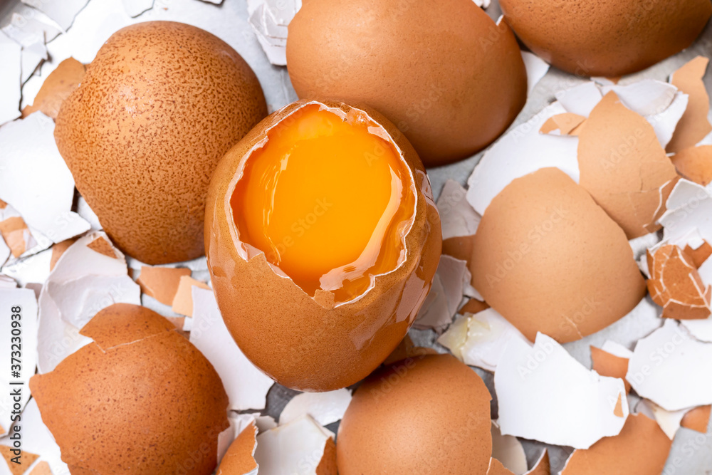 The cracked egg sees the yolk inside placed on a broken eggshell slice. Stock Photo Adobe Stock