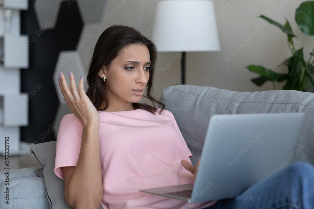 Unhappy young Arabic indian woman sit on couch at home use laptop have slow internet connection problems, disappointed ethnic female frustrated by online spam or virus on web on computer gadget Unhappy young Arabic indian woman sit on couch at home use laptop have slow internet connection problems, disappointed ethnic female frustrated by online spam or virus on web on computer gadget