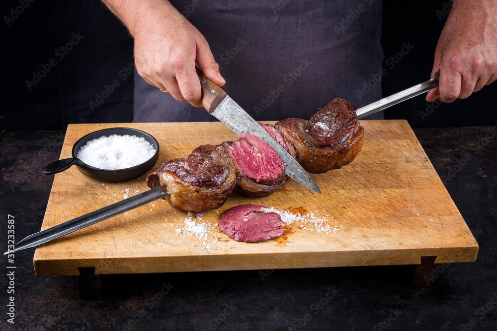 Traditional barbecue dry aged wagyu Brazilian picanha from the sirloin cap of rump beef sliced by a chef directly from the skewer as closeup on a wooden cutting board