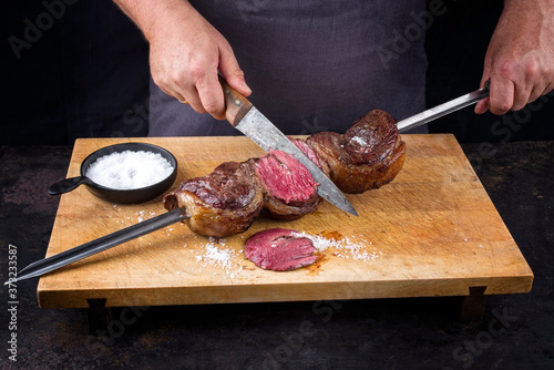 Traditional barbecue dry aged wagyu Brazilian picanha from the sirloin cap of rump beef sliced by a chef directly from the skewer as closeup on a wooden cutting board