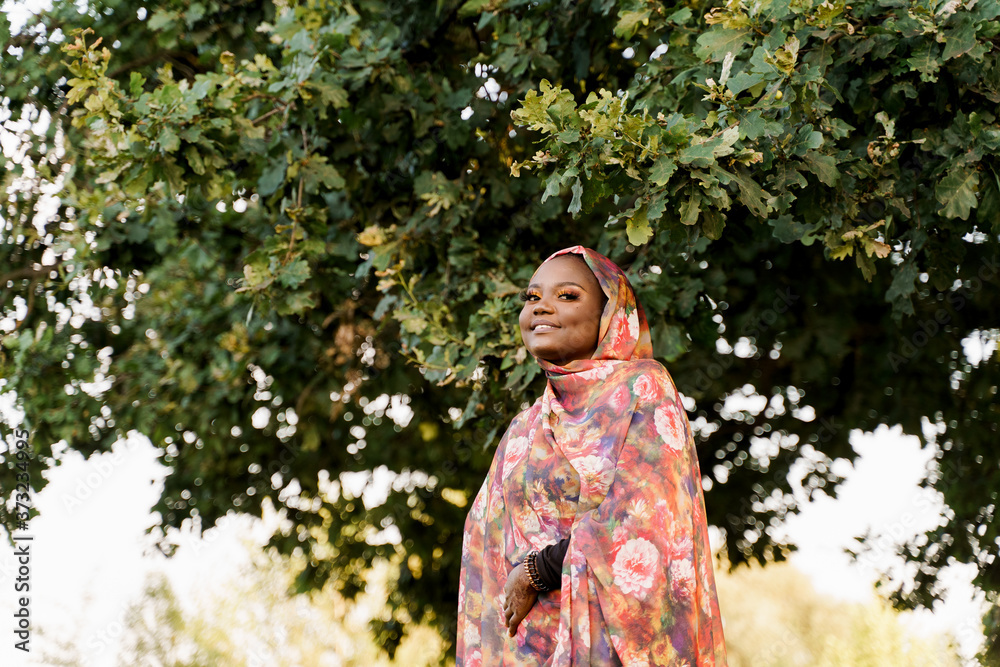 Muslim black woman African ethnicity weared traditional colorful hijab smiles under green tree. Arabic islam religion clothes. Pretty black girl smiles. Business for black woman. Muslim black woman African ethnicity weared traditional colorful hijab smiles under green tree. Arabic islam religion clothes. Pretty black girl smiles. Business for black woman.